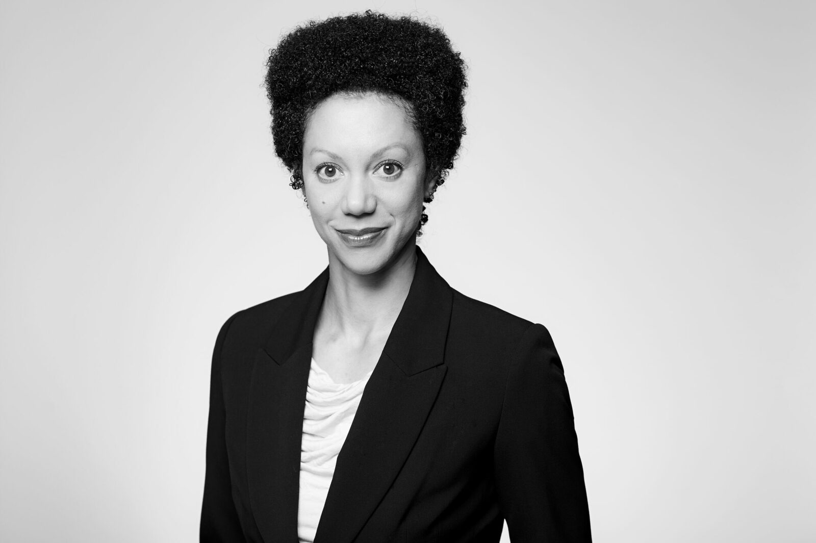 Professional black and white portrait of a female lawyer at our Hamilton, Ontario law firm. She is distinguished by her curly hair, dons a smart blazer and light-coloured blouse, her gentle smile reflecting the welcoming nature of our team.