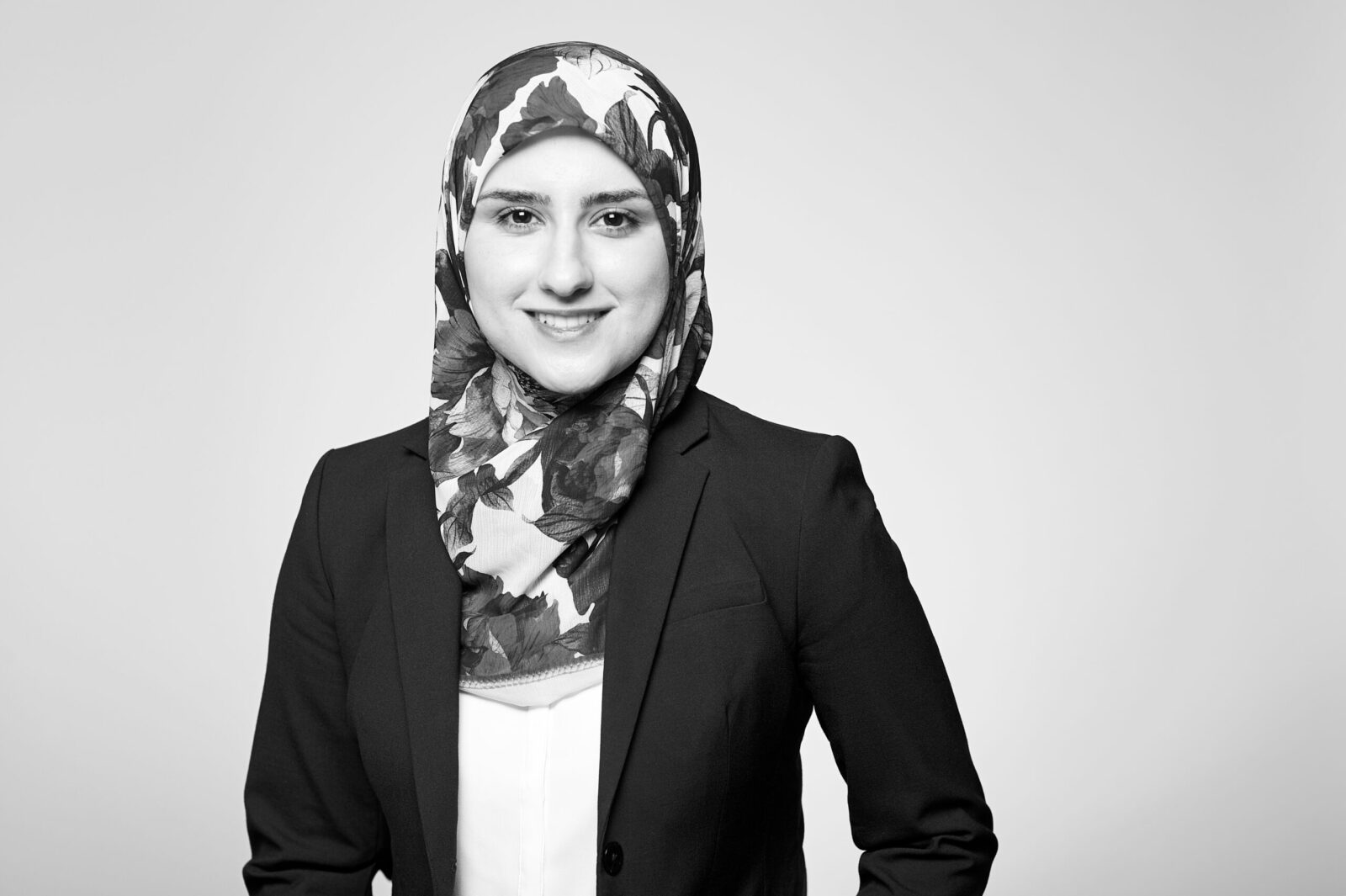 A professional woman, adorned in a business suit and patterned hijab denoting her association with our reputable law firm based in Hamilton, Ontario, offers a friendly smile towards the camera.