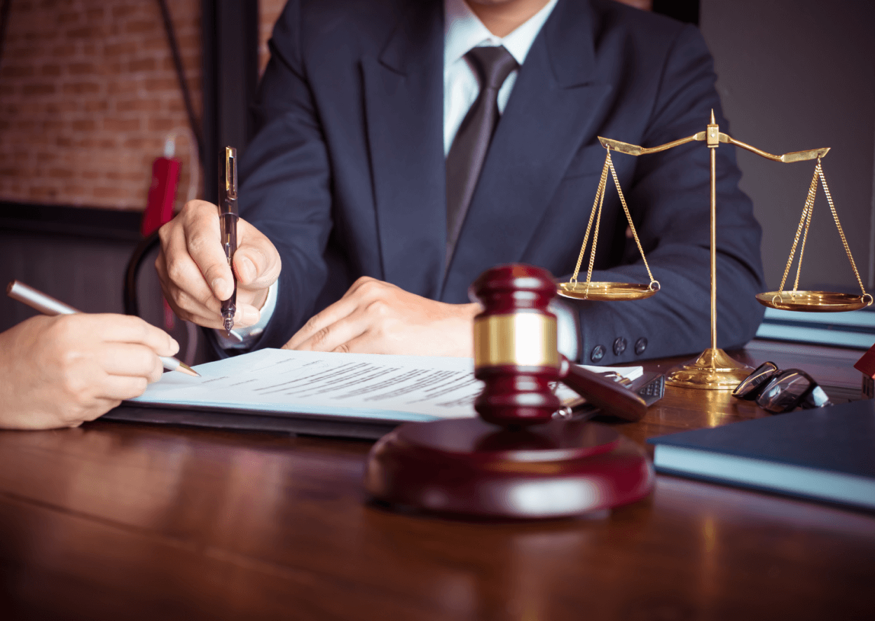 At our Hamilton, Ontario law firm, our expert legal professionals meticulously review documents at their desks, where symbolic items such as a gavel and scales of justice attest to our unfaltering commitment to fair and impartial legal practices.