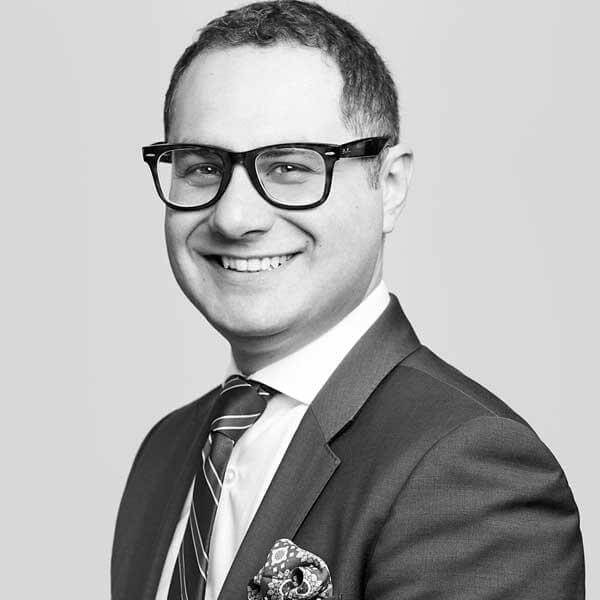 Professional attorney, distinctly characterized by a warm smile and glasses, smartly dressed in a suit and tie, rendering services at our distinguished Law Firm located in Hamilton, Ontario.
