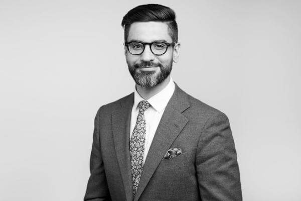 Professional gentleman, attired impeccably with a beard and glasses, featuring in a refined black and white portrait on the premises of our Law Firm situated in Hamilton Ontario.