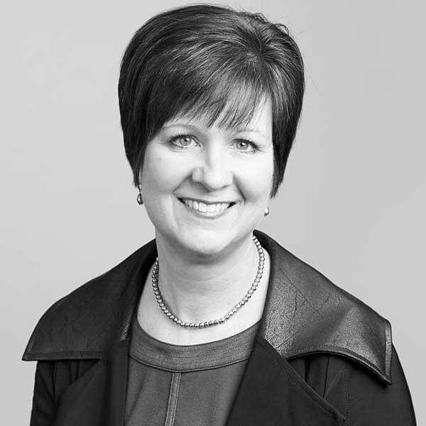 A professional black-and-white headshot portrays a cheerful woman with short hair from our Hamilton, Ontario law firm. She radiates confidence in her leather jacket and necklace.