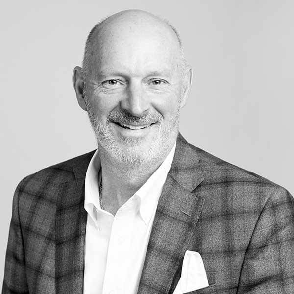 Featuring a distinguished gentleman with a bald head and beard, specializing in law firm practices within Hamilton Ontario. His professional attire of a checkered jacket over a crisp white shirt reflects his dedication to his profession. His helpful demeanor is captured in his warm smile, presented in an elegant black and white portrait.