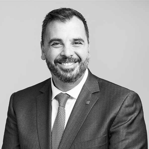 Professional attorney, impeccably dressed in a suit, offering a warm smile for a black and white portrait at our premier law firm based in Hamilton, Ontario.