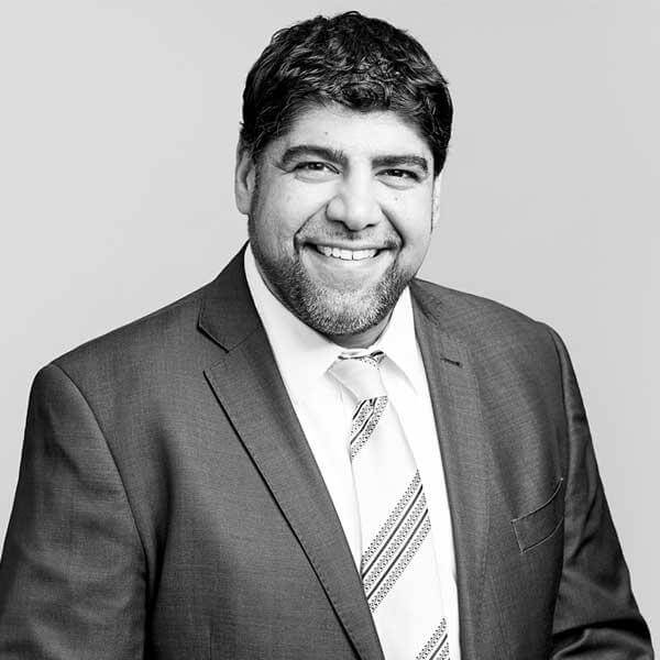 Professional monochrome portrait of a well-dressed man, featuring a confident smile indicative of our law firm's approachable yet formidable nature, proudly serving Hamilton, Ontario.