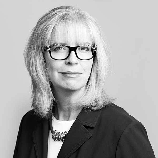 Distinguished female lawyer, donned in a sleek black blazered attire, with prescise eyeglasses illuminated against a refined gray backdrop, expertly symbolizing our esteemed Law Firm situated in Hamilton, Ontario.