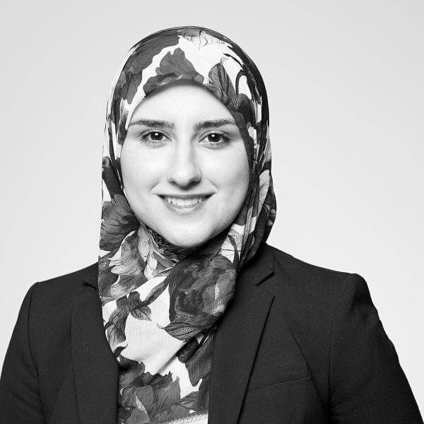 A professional monochrome photograph showcases a cheerful woman donned in a hijab and a business suit, epitomizing our diverse team at our Hamilton, Ontario based law firm.