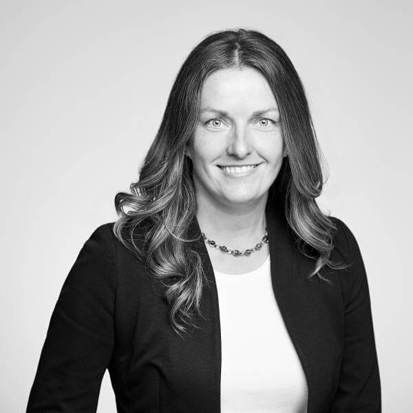 Professional black and white portrait of a cheerful female legal professional from our Hamilton, Ontario law firm, depicted with medium-length hair, elegantly styled in a blazer and complemented with a necklace.