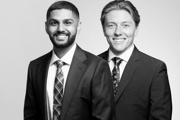 A professional black and white portrait featuring two congenially smiling attorneys from our esteemed Law Firm, situated in Hamilton, Ontario, embodying the perfect blend of expertise and approachability.